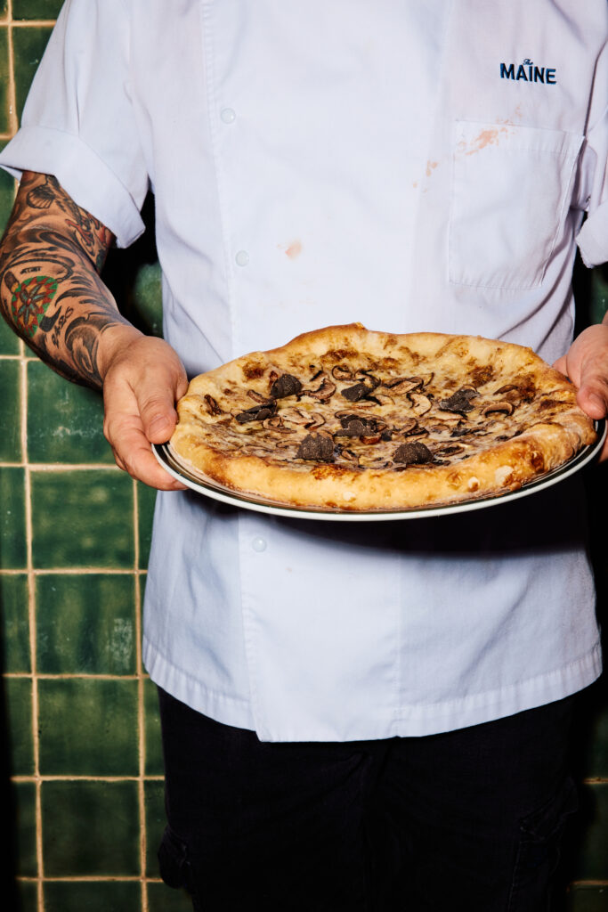 Chef with tattoos holding truffle pizza  at The Maine 